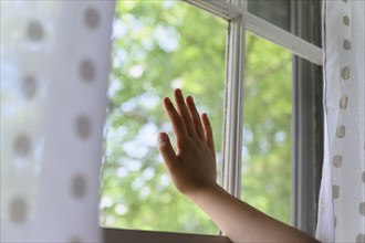 Child's hand touching window with trees behind,,
