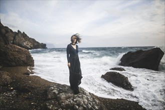 Ukraine, Crimea, Young woman standing on rocky beach