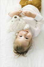 Smiling toddler girl lying on bed with teddy bear toy