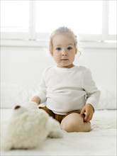Smiling toddler girl sitting on bed with teddy bear toy