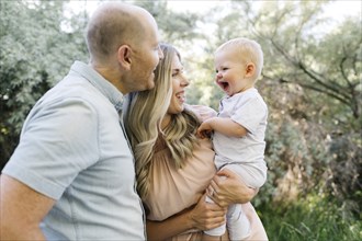 Happy parents with baby son laughing in garden