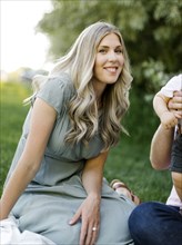 Outdoor portrait of smiling woman sitting o grass with her family nearby