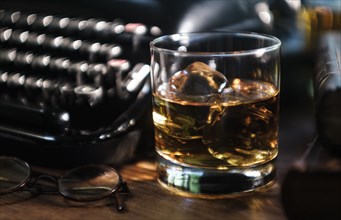 Whiskey glass next to typewriter on desk