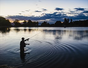USA, Utah, Salem, Silhouette of man fly fishing in lake at dusk