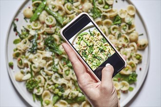 Woman's hand photographing orecchiette with smartphone
