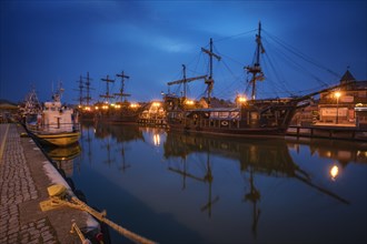Poland, Pomerania, Leba, Historic tall ships moored at harbour at dusk