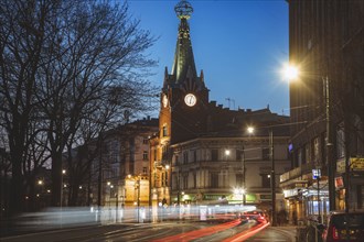Poland, Lesser Poland, Krakow, Illuminated city street with clock tower at night