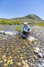 USA, Idaho, Sun Valley, Woman sitting on rock in river