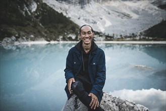 Italy, South Tyrol, Cortina d Ampezzo, lake Sorapis, Portrait of young man sitting on rock at mountain lake