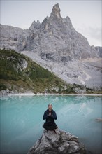 Italy, South Tyrol, Cortina d Ampezzo, lake Sorapis, Man in meditation pose sitting on rock against lake