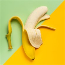 Half peeled banana on green and yellow background