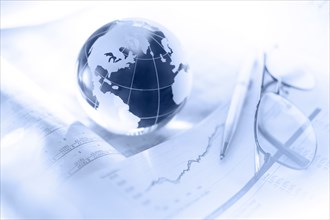 Glass globe with pen and glasses on financial charts