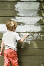 Boy (4-5) painting cottage wall
