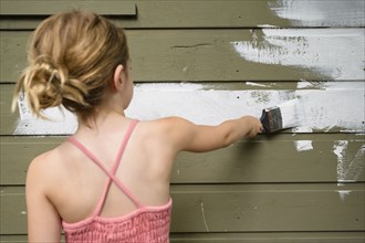 Girl (6-7) painting cottage wall