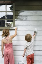 Girl (6-7) and boy (4-5) painting cottage wall