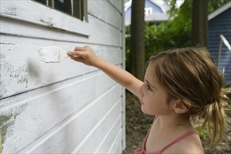 Girl (6-7) painting cottage wall