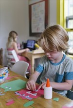 Boy (4-5) preparing paper cutout, girl (6-7) in background