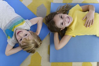 Overhead portrait of boy (4-5) and girl (6-7) lying on yoga mats