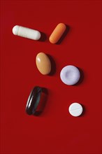 Various pills and capsules on red background