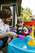 Father and toddler daughter (2-3) playing with water in garden
