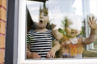 Portrait of toddler girl (2-3) and baby boy (18-23 months) standing behind window
