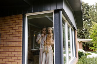 Mother with baby son (18-23 months) standing behind window
