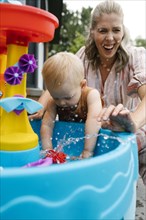 Mother with baby son (18-23 months) playing with water in garden