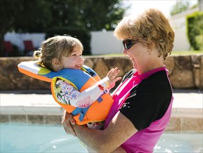 Grandmother holding toddler girl (2-3) on outdoor swimming pool