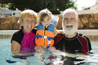 Portrait of grandparents with toddler girl (2-3) standing in outdoor swimming pool