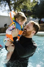 Father playing with toddler daughter (2-3) in outdoor swimming pool