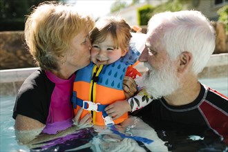 Grandparents with toddler girl (2-3) standing in outdoor swimming pool