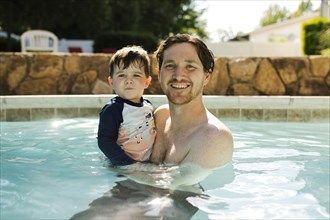 Portrait of father with toddler son (2-3) standing in outdoor swimming pool