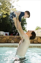 Father playing with toddler son (2-3) in outdoor swimming pool