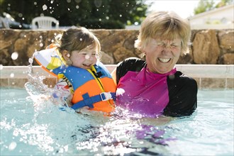 Grandmother playing with toddler girl (2-3) in outdoors swimming pool