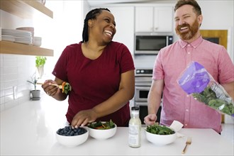 Happy man and woman preparing salad in kitchen