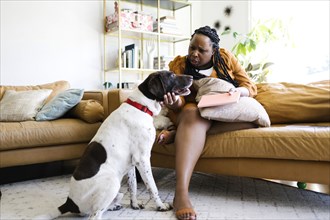 Woman sitting on sofa and stroking her dog