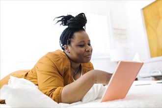 Smiling woman lying on bed and using tablet