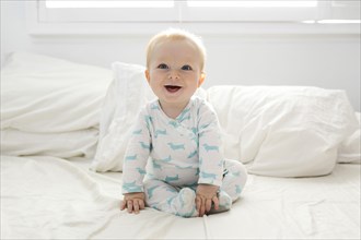 Smiling baby boy (6-11 months) sitting on bed