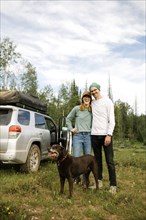 USA, Utah, Uinta National Park, Portrait of smiling couple with dog standing in meadow, off road car in background