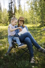 USA, Utah, Uinta National Park, Mother and daughter (6-7) doing crossword in meadow in forest