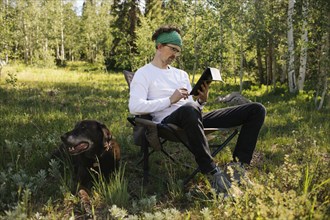 USA, Utah, Uinta National Park, Man with dog sitting in meadow in forest, using tablet