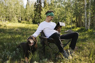 USA, Utah, Uinta National Park, Man with dog sitting in meadow in forest, using tablet