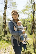 USA, Utah, Uinta National Park, Portrait of smiling woman with baby son (6-11 months) in baby carrier in forest
