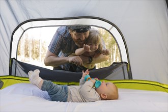 USA, Utah, Uinta National Park, Father and daughter (2-3) peeking into tent and looking at baby boy (6-11 months) inside