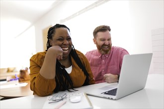 Smiling man and woman looking at laptop at desk in home office