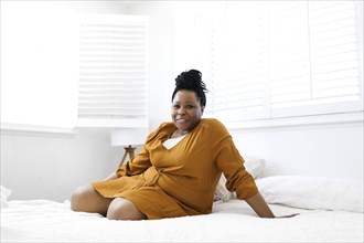 Portrait of smiling woman in orange dress sitting on bed