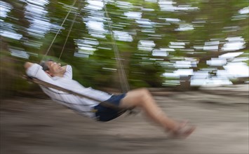 Senior man swinging on tropical beach, blurred motion