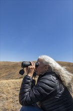 USA, Idaho, Bellevue, Senior woman looking through binoculars in desert