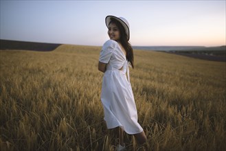 France, Young woman in white dress standing in cereal field