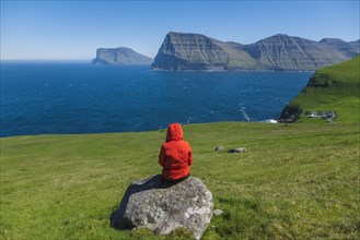 Denmark, Faroe Islands, Klaksvik, Trollanes, Woman sitting on rock and looking at ocean